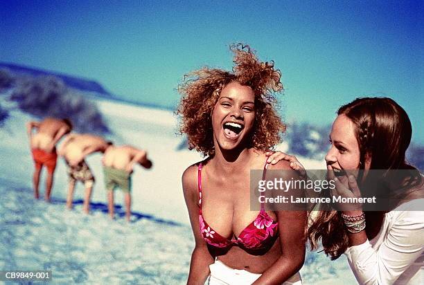 two women on beach, laughing at men showing buttocks - women mooning stockfoto's en -beelden
