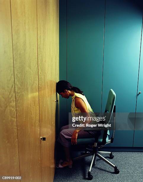 young woman on office chair, banging head against wall - banging your head against a wall stock pictures, royalty-free photos & images