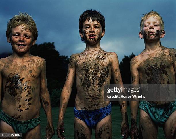 three boys covered in mud in front of a lake - covering stock-fotos und bilder