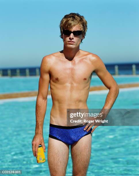 young man standing by swimming pool, holding can, portrait - calções de corrida imagens e fotografias de stock