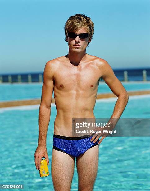 young man standing by swimming pool, holding can, portrait - young men in speedos 個照片及圖片檔