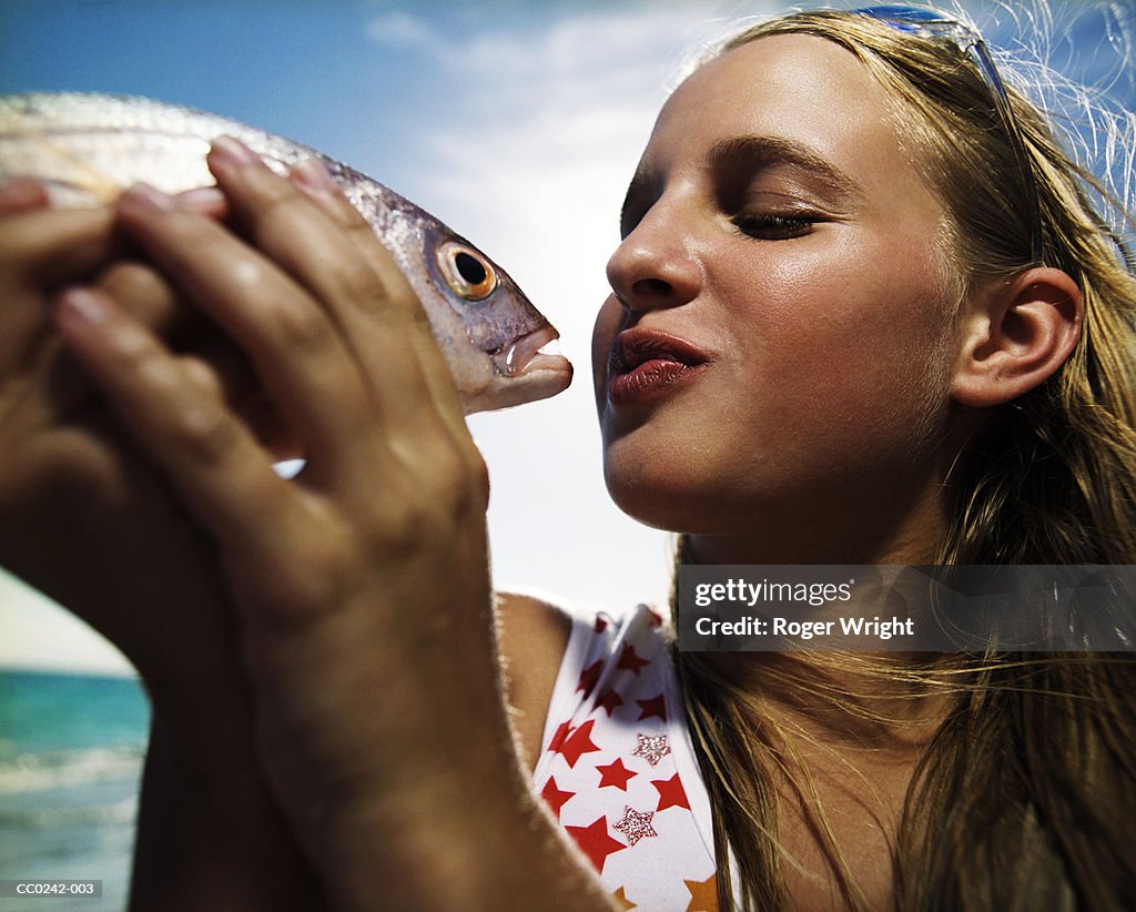 Teenage girl (13-15) holding up fish to kiss, close-up