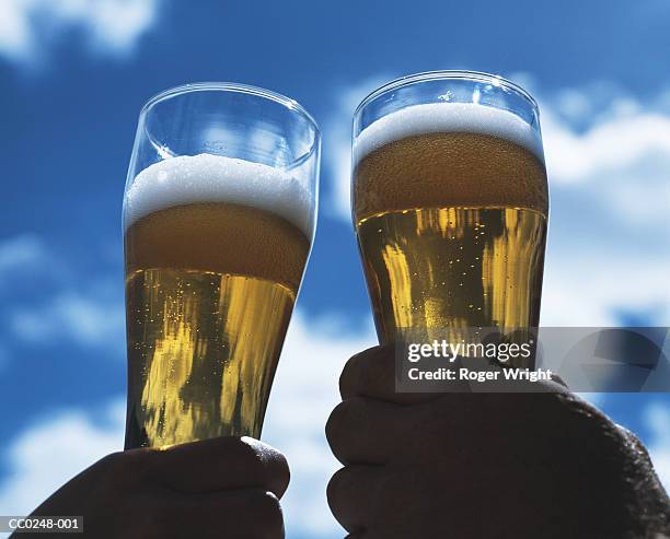 two men outdoors raising a toast with glasses of beer, close-up - biergarten stockfoto's en -beelden