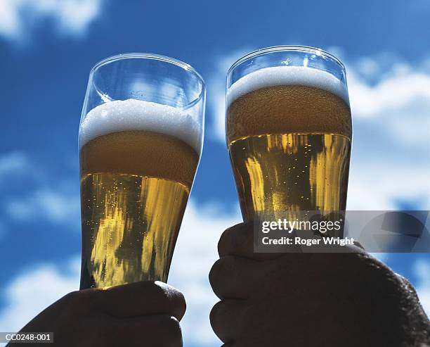 two men outdoors raising a toast with glasses of beer, close-up - cheers beer stock pictures, royalty-free photos & images