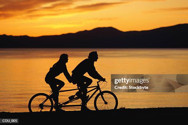 silhouette of two people on bike - tandem ストックフォトと画像