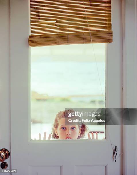 girl (5-7) peering through window in door, portrait - girl looking through window stock pictures, royalty-free photos & images