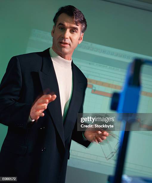 man holding glasses and gesturing; chart on screen behind him - slide projector stock pictures, royalty-free photos & images