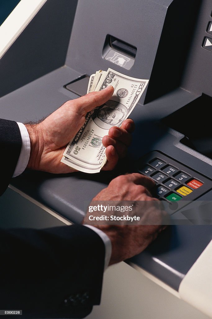 Hands holding money and using bank machine