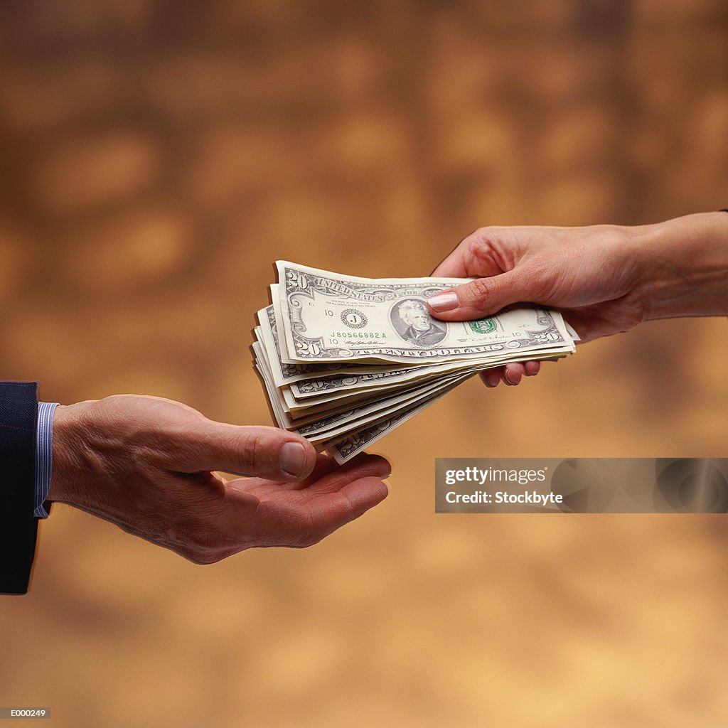 Woman's hand giving stack of US $20 bills to man's hand