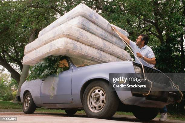 man fastening four mattresses to roof of car - car roof stock pictures, royalty-free photos & images