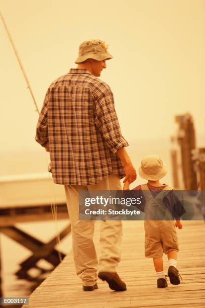 father walking on pier with son, carrying fishing pole - carrying pole stock pictures, royalty-free photos & images