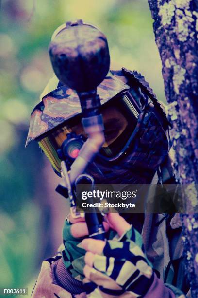 man in fatigues with paintball gun hiding behind tree - rifle sight stock pictures, royalty-free photos & images