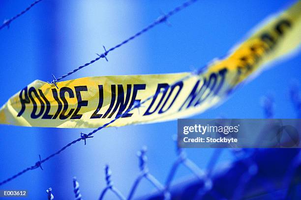 yellow police tape on barbed wire chain link fence - restricted area sign stock-fotos und bilder