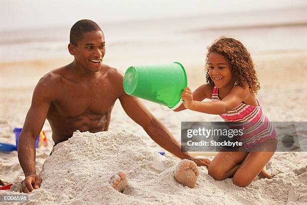 girl burying dad in sand - bury fotografías e imágenes de stock