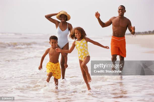 african american family running along beach - bermuda shorts stock pictures, royalty-free photos & images