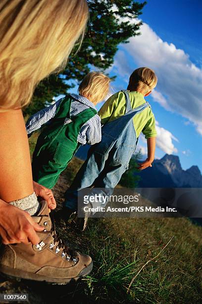 mother tying boot for hike, children walking ahead - get ahead stock-fotos und bilder
