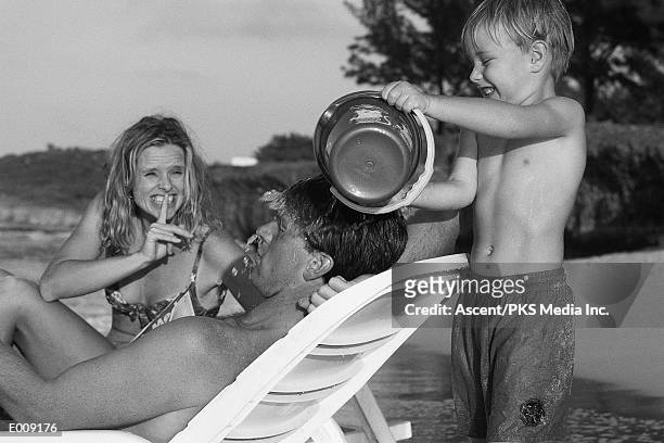 boy pouring water on father's head - sand pail and shovel stock pictures, royalty-free photos & images
