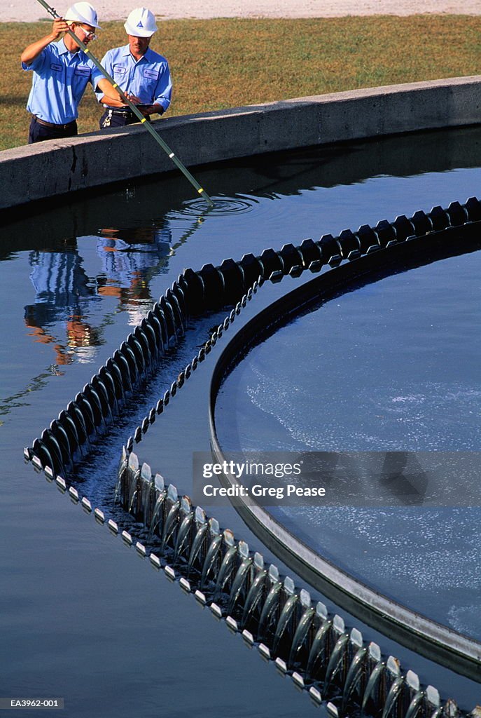 Men sampling water from clarifier tank at waste treatment plant