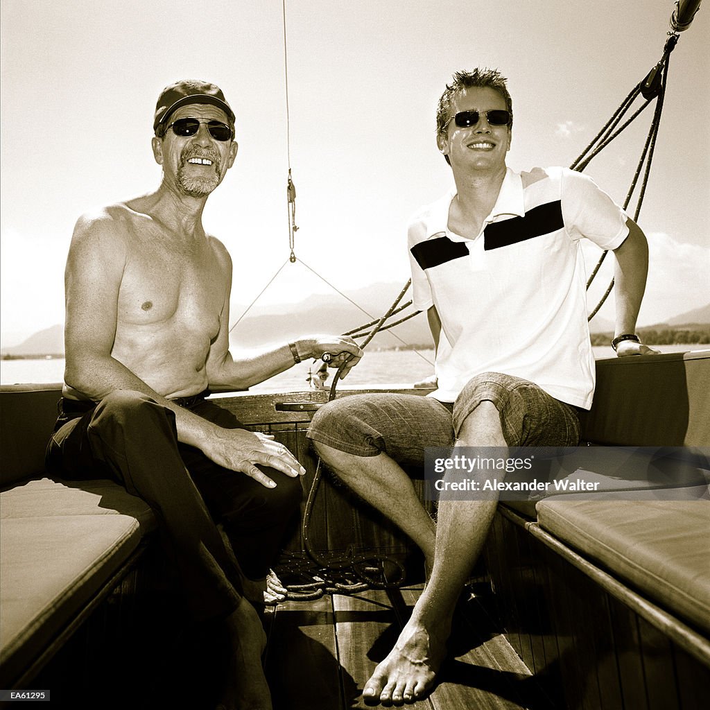 Young man and father at back of sailboat, wearing sunglasses (B&W)