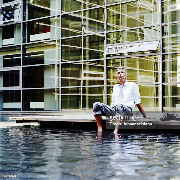 businessman sitting outdoors, feet in pool of water - rolled up pants stockfoto's en -beelden