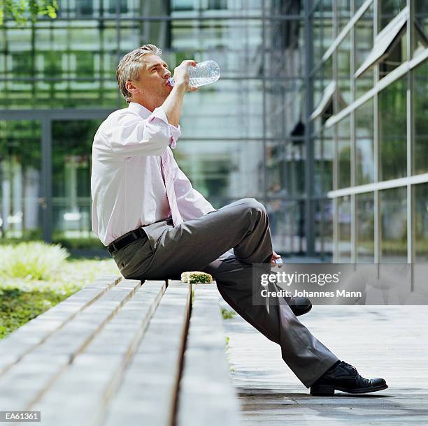 businessman drinking bottle of water outdoors - mann anzug gebäude objekt draussen stock-fotos und bilder