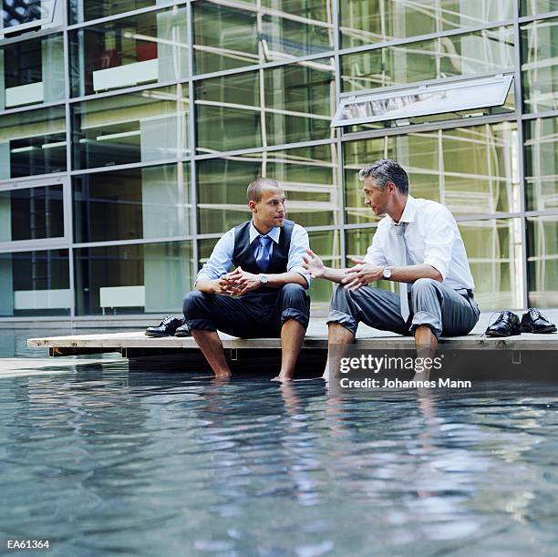 two businessmen sitting outdoors, feet in pool of water - mann fotografías e imágenes de stock