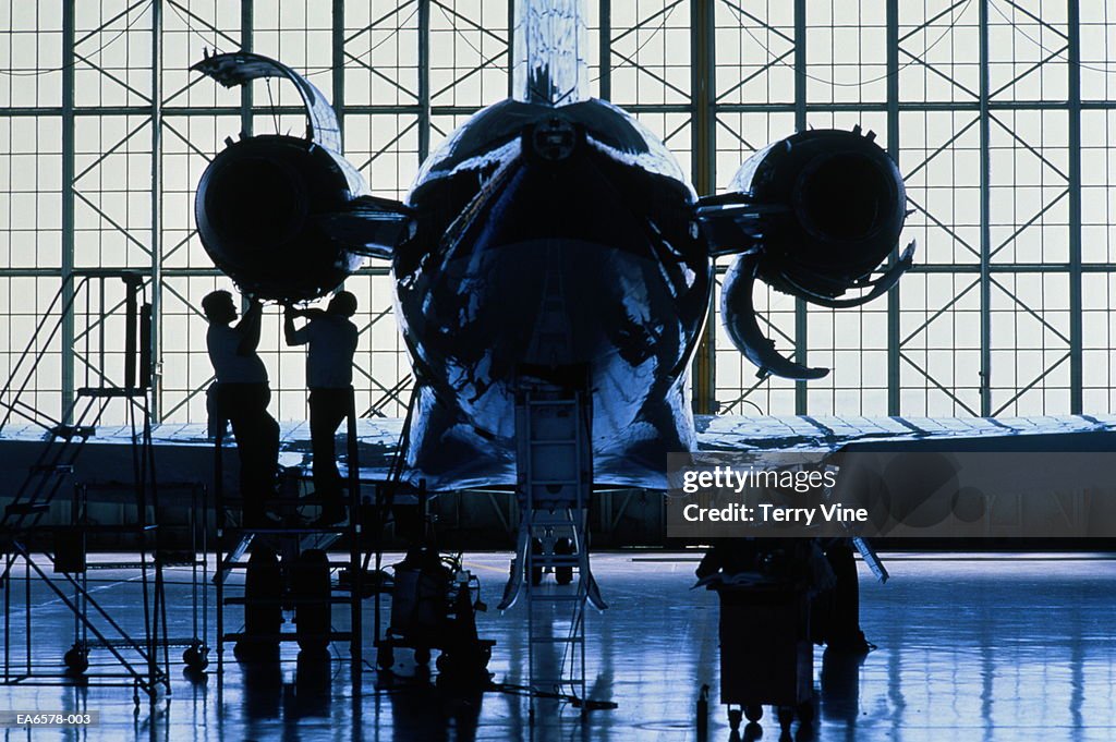 Engineers working on passenger aircraft engine, rear view