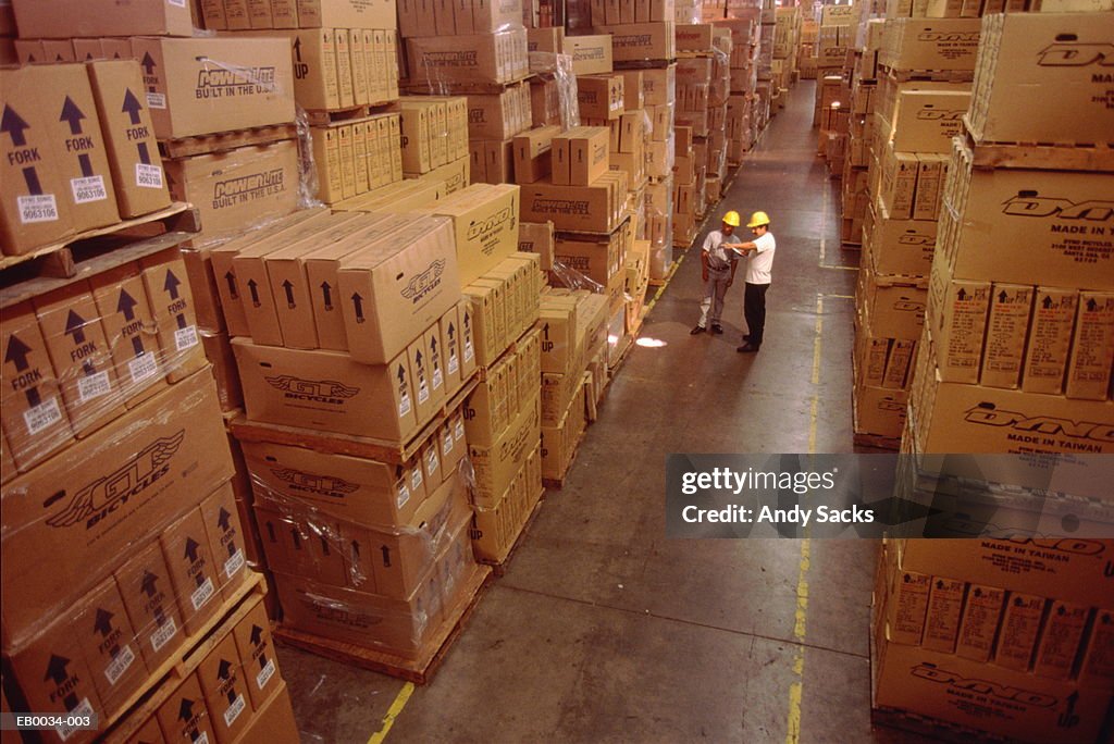 Two workers talking in aisle of warehouse, elevated view