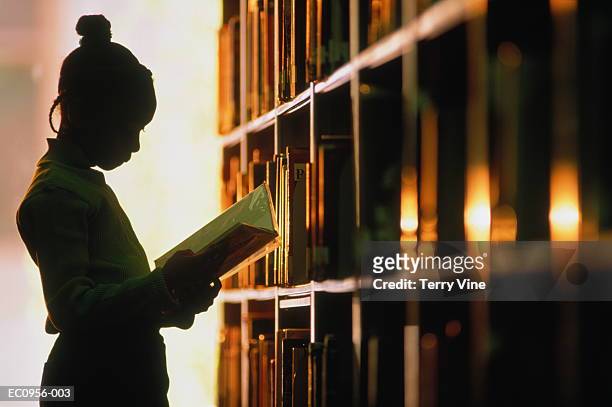 girl (6-8) looking at book in library, silhouette - girl silhouette stockfoto's en -beelden