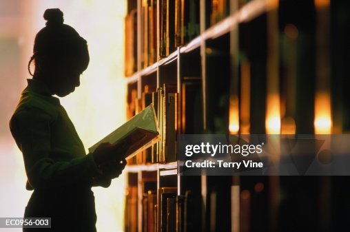 Girl (6-8) looking at book in library, silhouette Girl (6-8) looking at book in library, silhouette