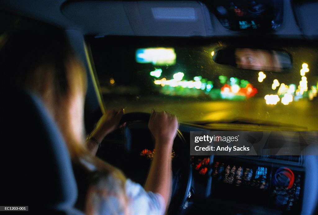 Young woman driving car at night, interior view (blurred motion)