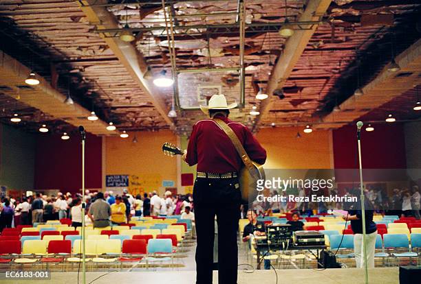 man wearing cowboy hat, playing guitar in auditorium, rear view - country and western music stock-fotos und bilder