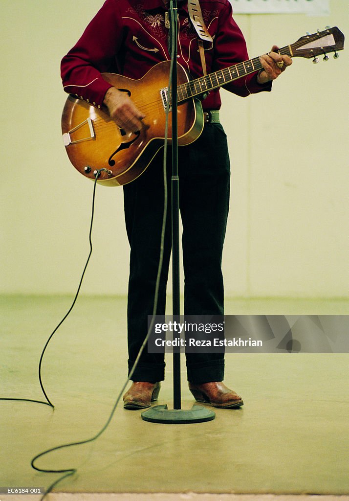 Man playing guitar in front of mircrophone stand