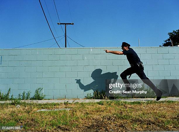 policeman running next to cement wall, yelling and pointing finger - 追う ストックフォトと画像