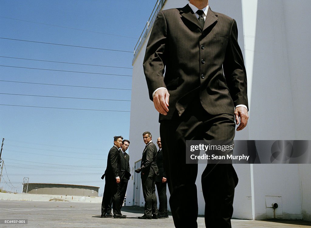 Businessmen standing outside building, one walking away