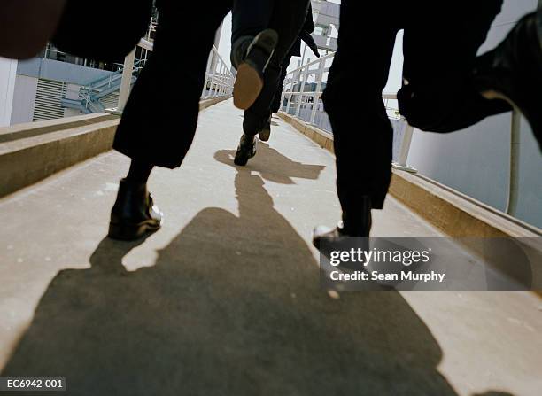 men in black suits running on walkway, low angle view - achtervolgen stockfoto's en -beelden