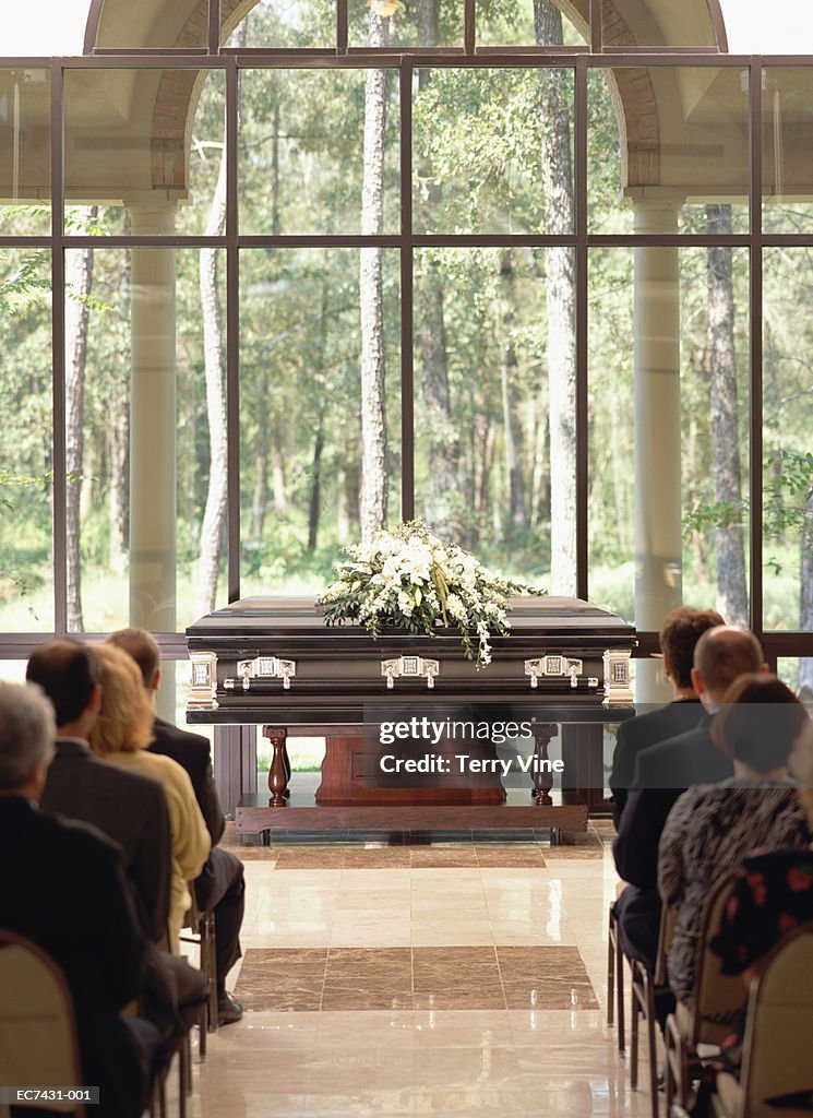 Group of people sitting at funeral, casket with flowers in front
