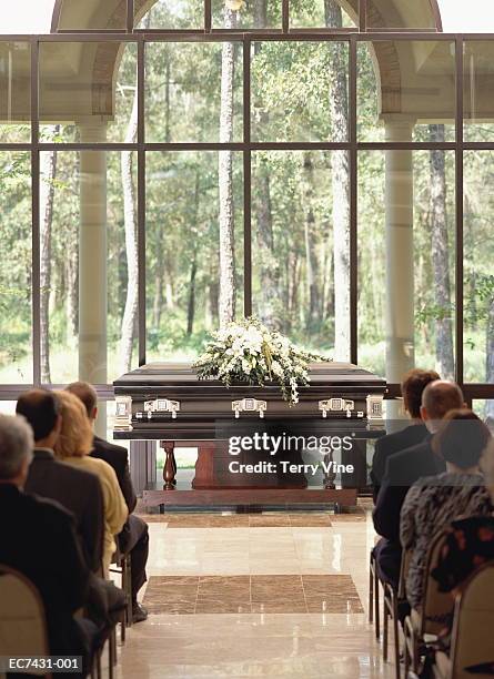 group of people sitting at funeral, casket with flowers in front - funeral stockfoto's en -beelden