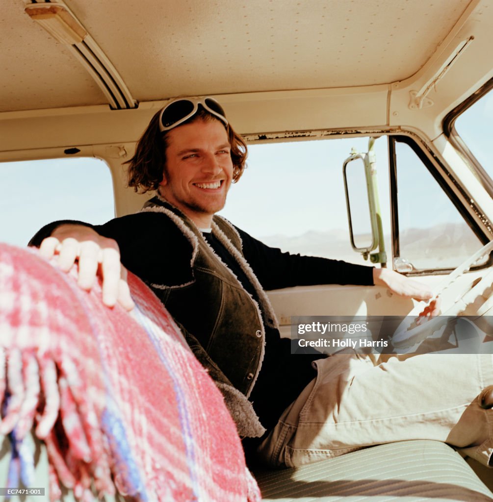 Young man sitting in front seat of van, smiling