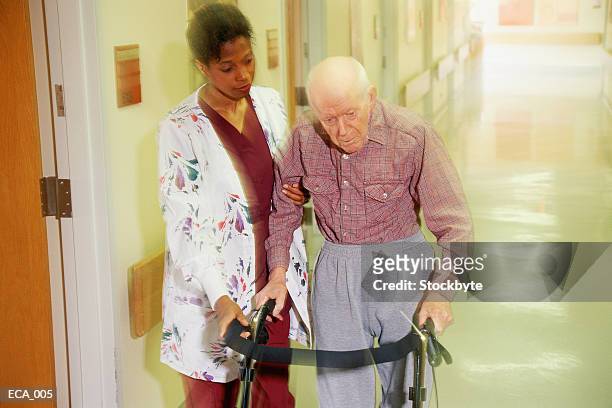 woman helping elderly man walk down hallway using walking frame - blank frame stockfoto's en -beelden