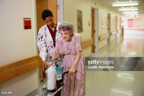 woman helping elderly woman with walker down corridor - oxygen cylinder stock pictures, royalty-free photos & images