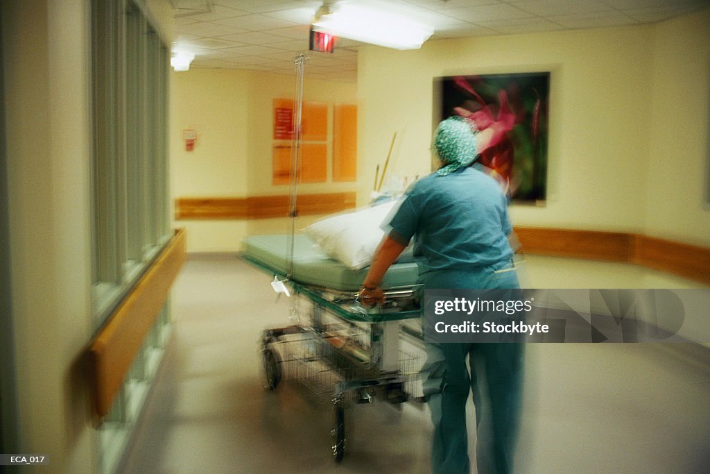 Hospital orderly pushing empty stretcher down corridor