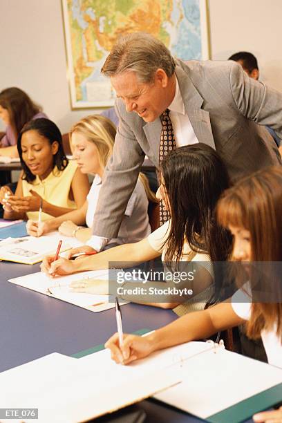 teacher leaning to check girl's work as she writes in notebook - check up ストックフォトと画像