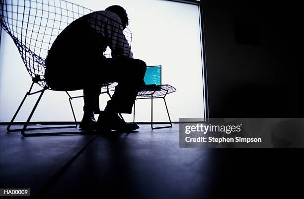 young man on wire-framed chair using laptop computer, silhouette - stehen stock pictures, royalty-free photos & images