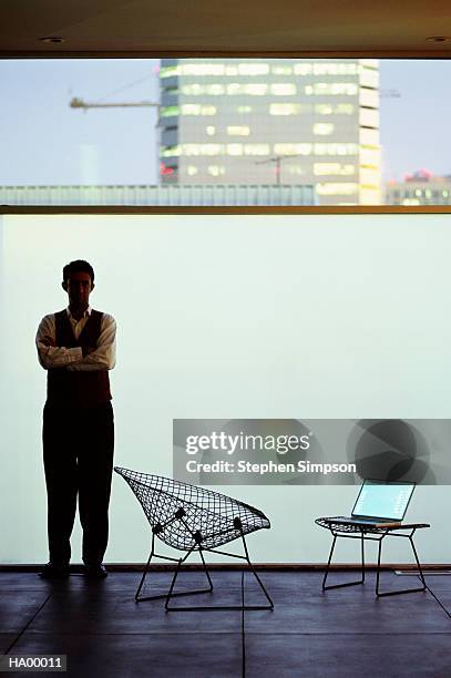 man standing beside wire-framed chair and laptop computer - stehen stock pictures, royalty-free photos & images