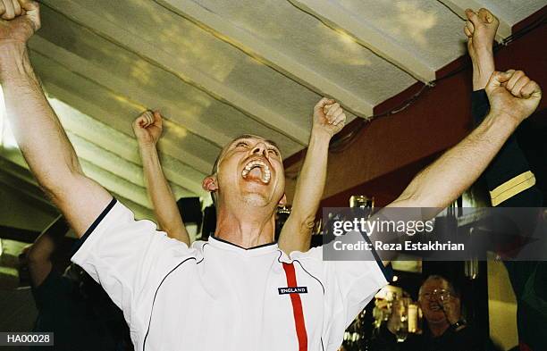 cheering football fan watching match in pub, arms raised, close-up - begeistert fernsehen stock-fotos und bilder