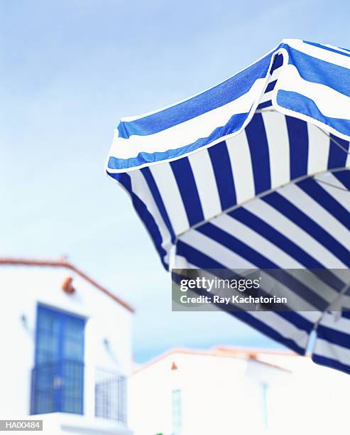 blue and white umbrella, houses in background - parasols stockfoto's en -beelden