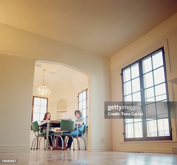 young couple sitting at kitchen table, man reading newspaper - garcia stockfoto's en -beelden