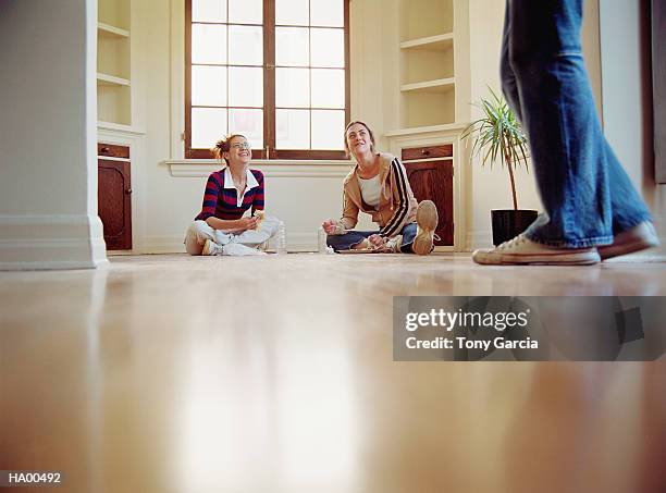 two young women eating on floor of empty house, laughing - garcia stockfoto's en -beelden