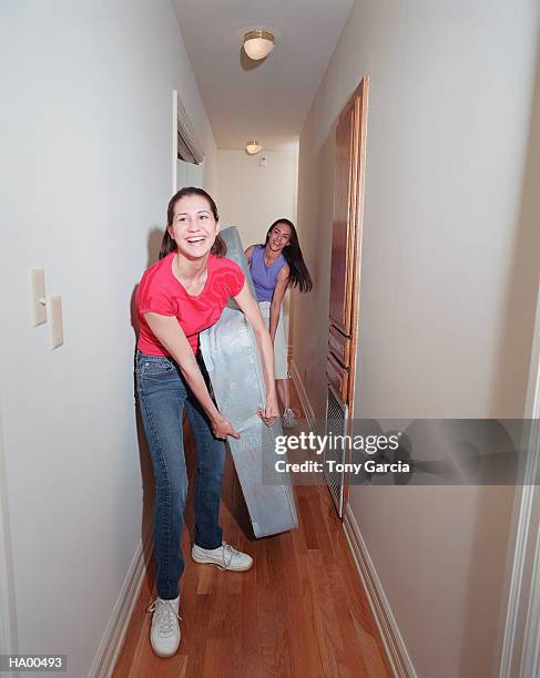 two young women moving mattress through hallway, laughing - garcia stockfoto's en -beelden